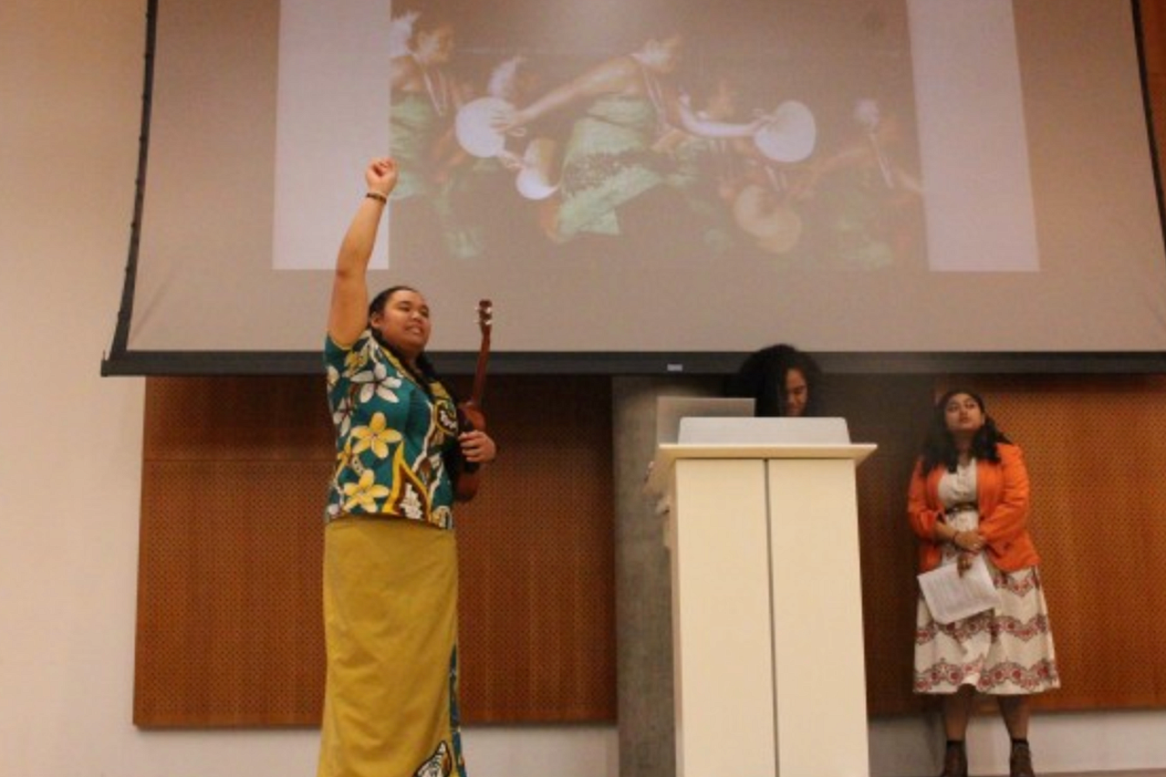 Women standing on stage raising her fist.