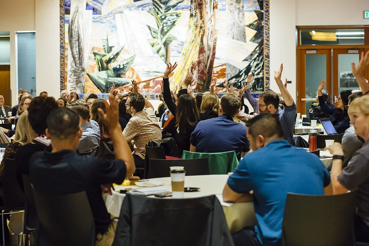 Seated faculty are raising their hands at an event.