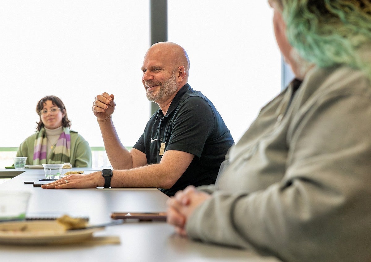 Man presenting in a writing workshop, sitting and smiling alongside two peers