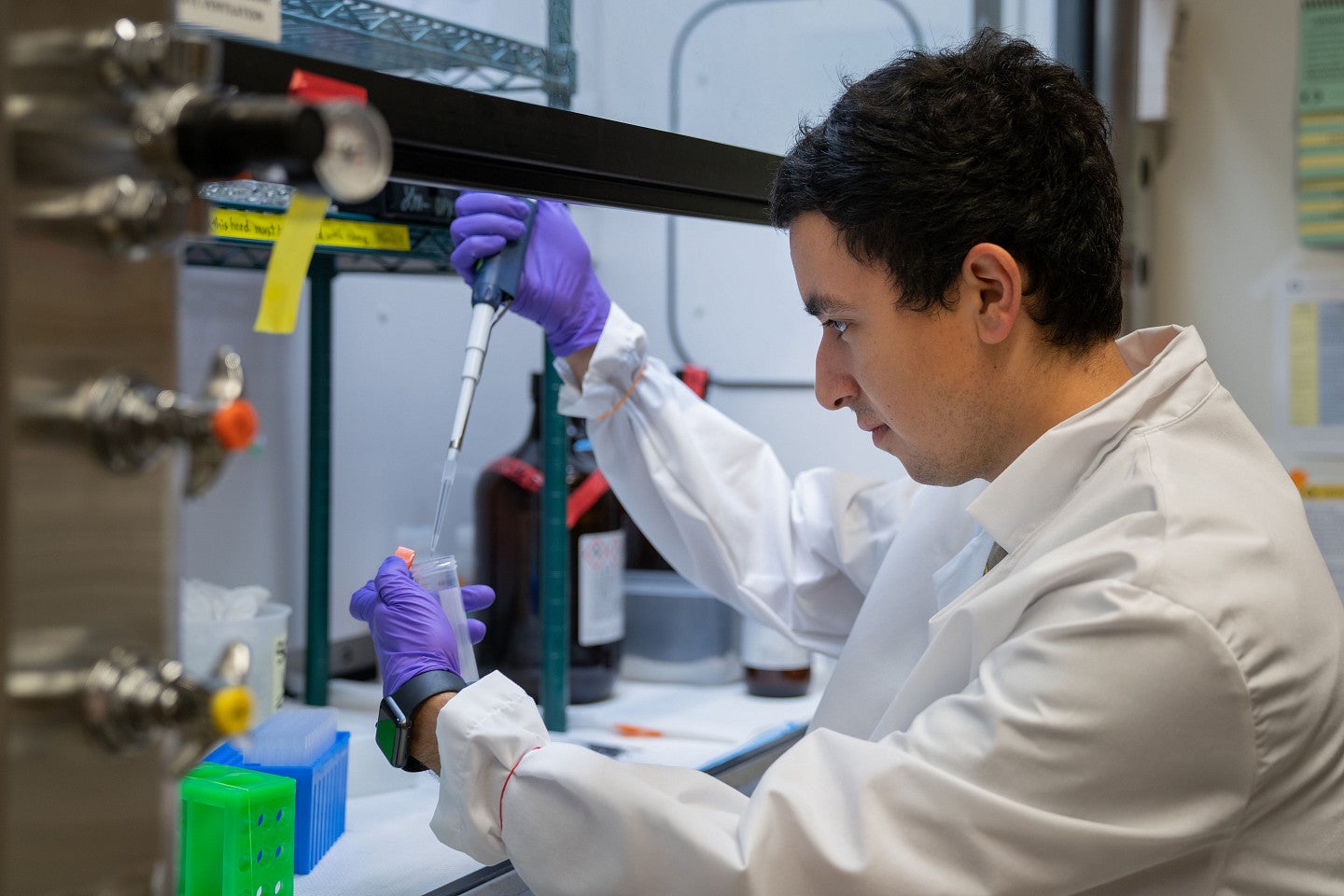 Student in lab in white coat and purple gloves holding test tube.