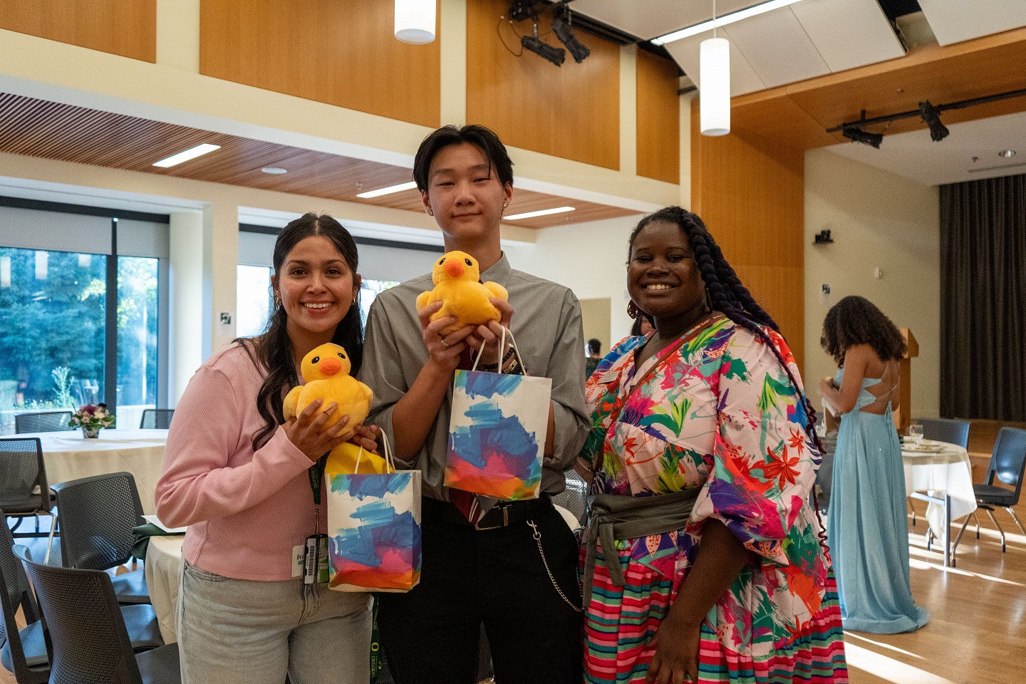 Two students holding Ducks with University psychologist wearing braids and a colorful dress.
