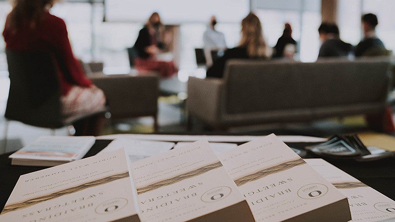 Braiding Sweetgrass books displayed on table in classroom with blurred people at desks behind