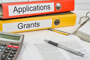 two notebooks one labeled application and other grants next to computer and notebook