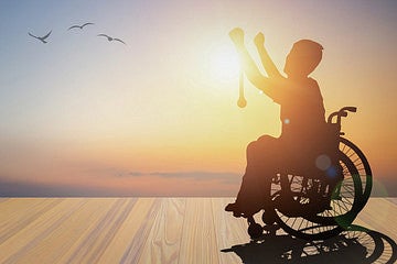 person using a wheelchiar with arms towards the sky against a sunrise